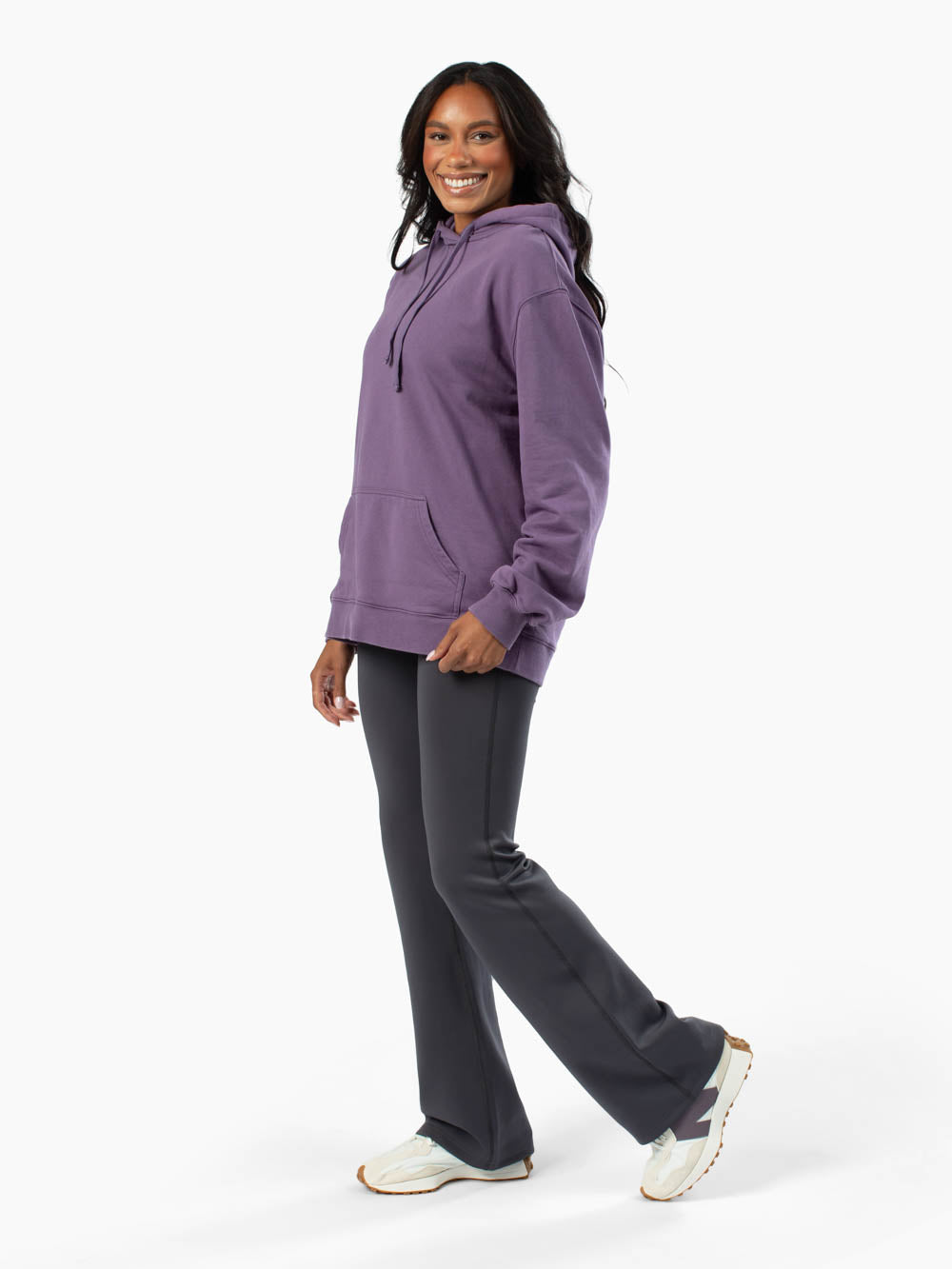Tall woman wearing a purple hoodie and gray flare leggings on a white background