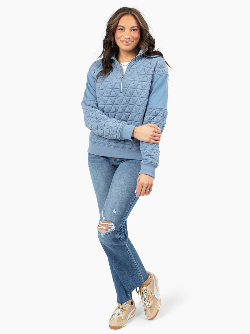 Tall woman wearing blue quilted half zip sweatshirt with jeans